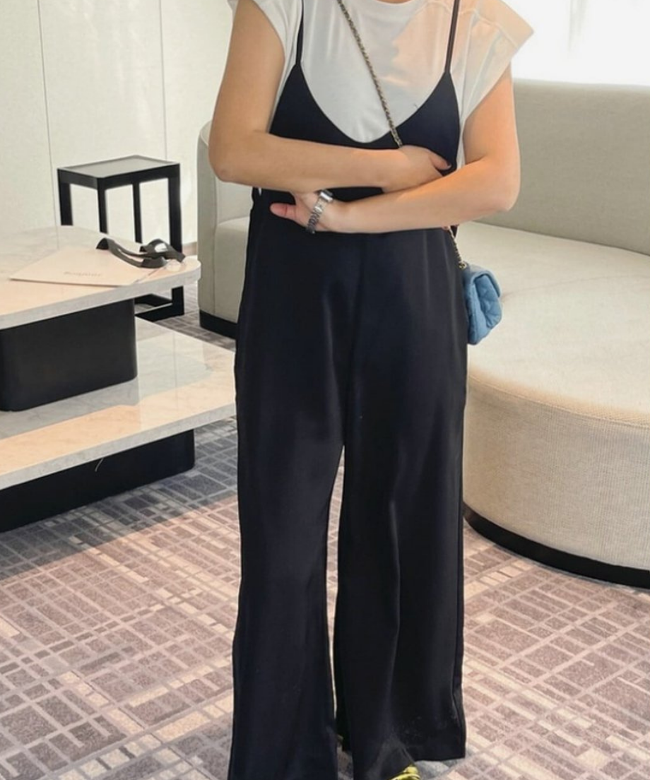 黒のキャミソールサロペットに白のパワーショルダーTシャツをインナーとして着用したが腕を組んだ女性の写真。