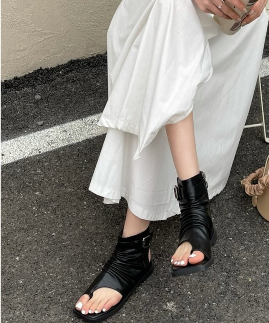 アスファルトの上で、黒のルーズなブーツサンダルを履いて座る女性の正面カット