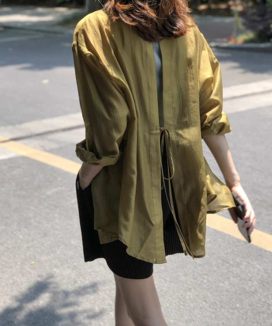 屋外でグリーンカラーのシアーシャツを着用した、背面スリットとリボンの動きがわかる後ろ姿。
