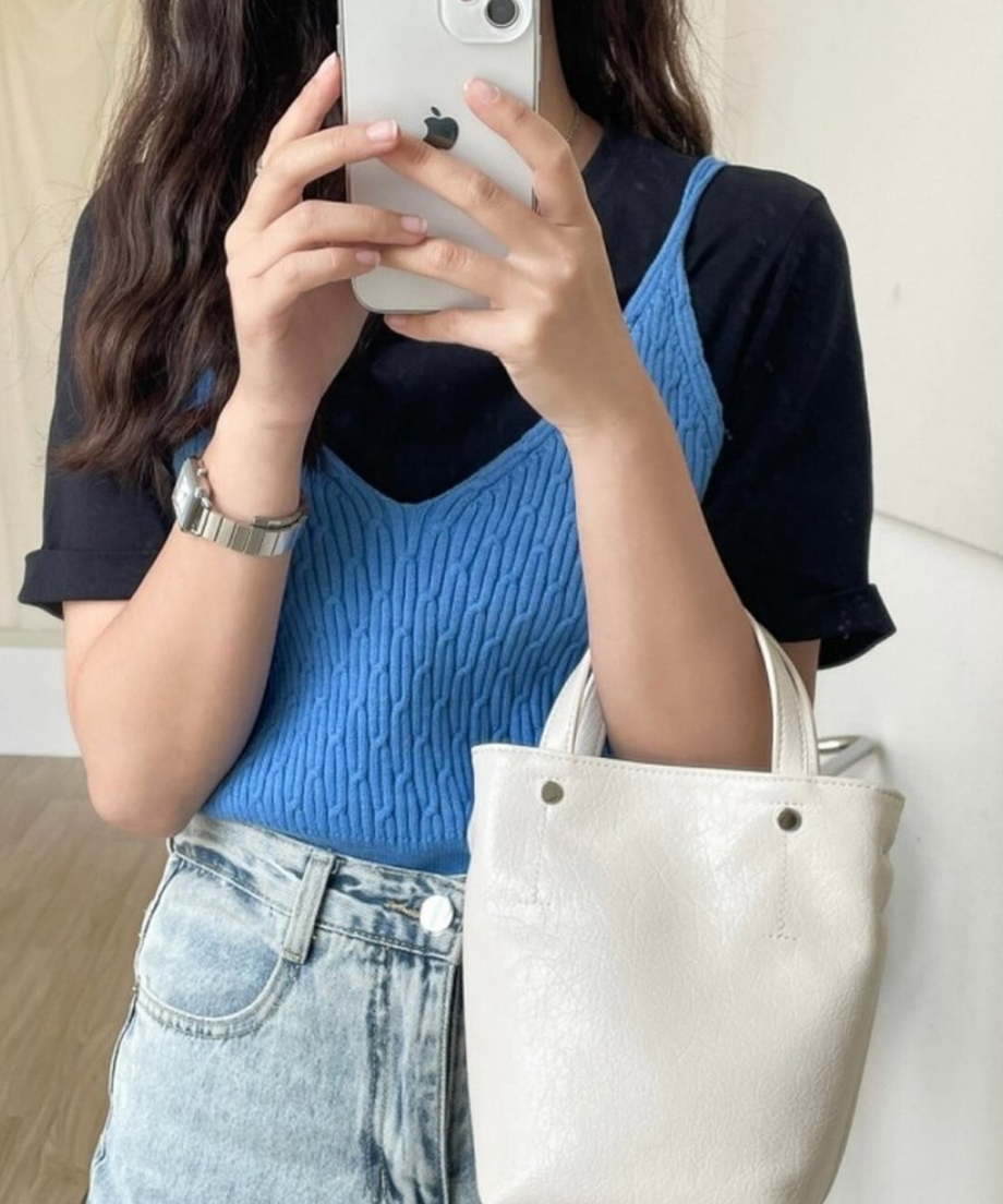 ホワイトのミニトートバッグを腕にかけ、スマートフォンで自撮りをするブルーのビスチェを着た女性