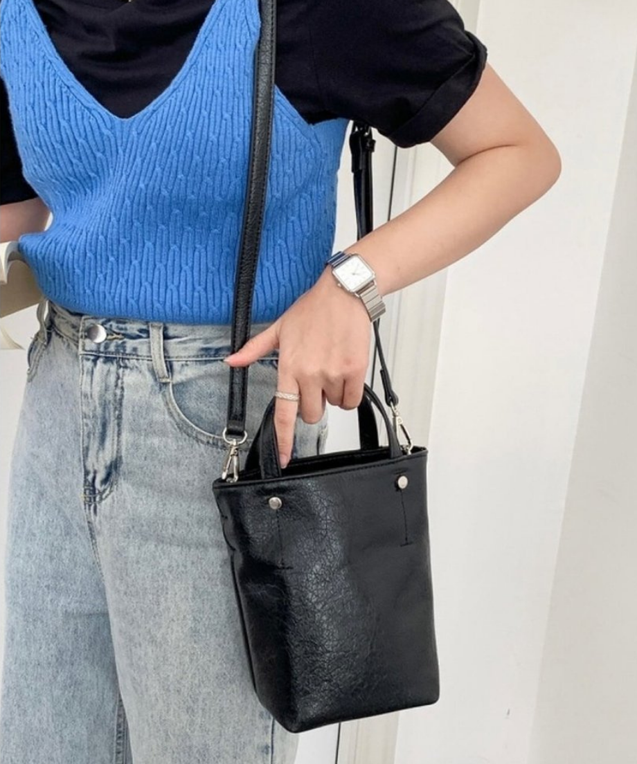 ブラックのミニトートバッグを斜め掛けにし、バッグの持ち手に指をかけるデニムスタイルの女性