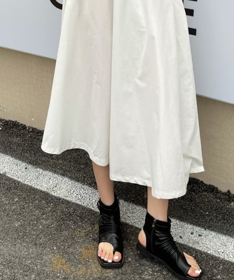 アスファルトの上で、黒のルーズなブーツサンダルを履いて立つ女性の正面カット