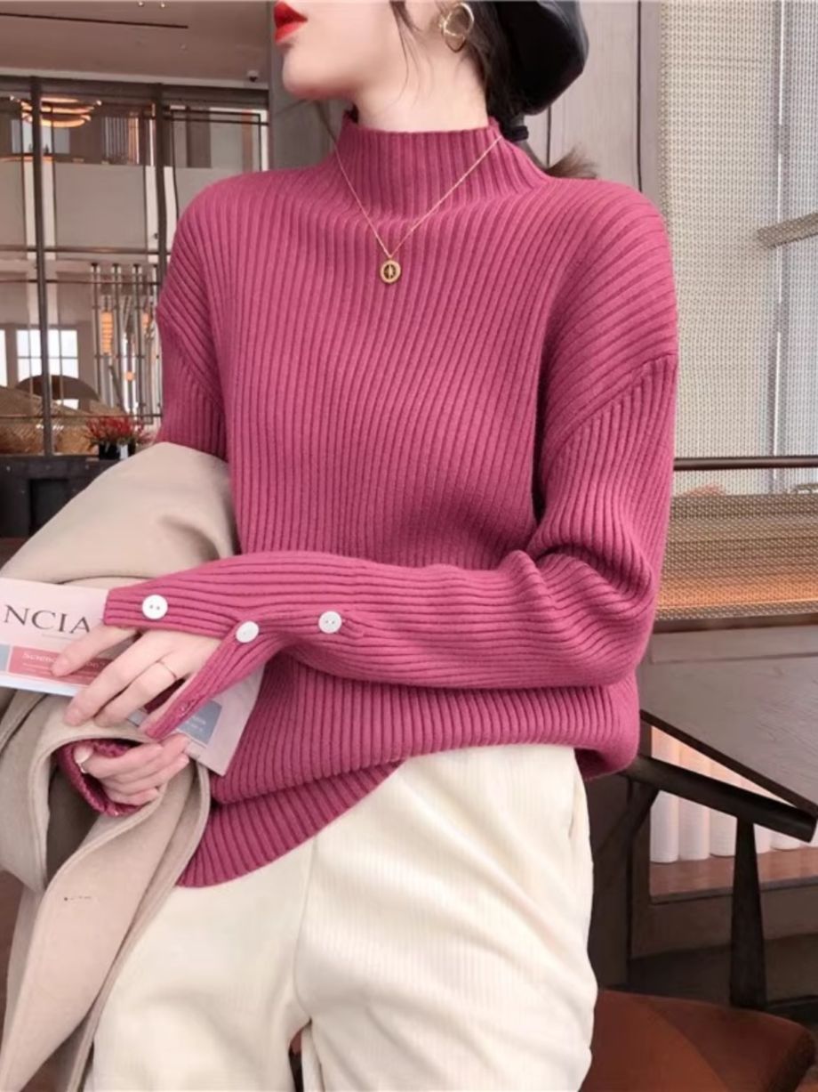マゼンタのモックネックニットを着用し、ベージュのコートを手に持っている女性のバストアップ。モックネックと袖ボタンが見える。