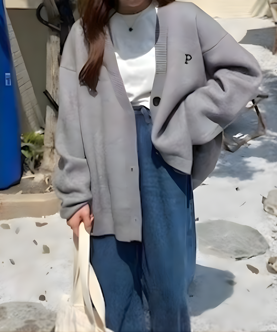 グレーのオーバーサイズカーディガンを白いTシャツとパンツに合わせ、屋内でポーズをとる女性の全身。