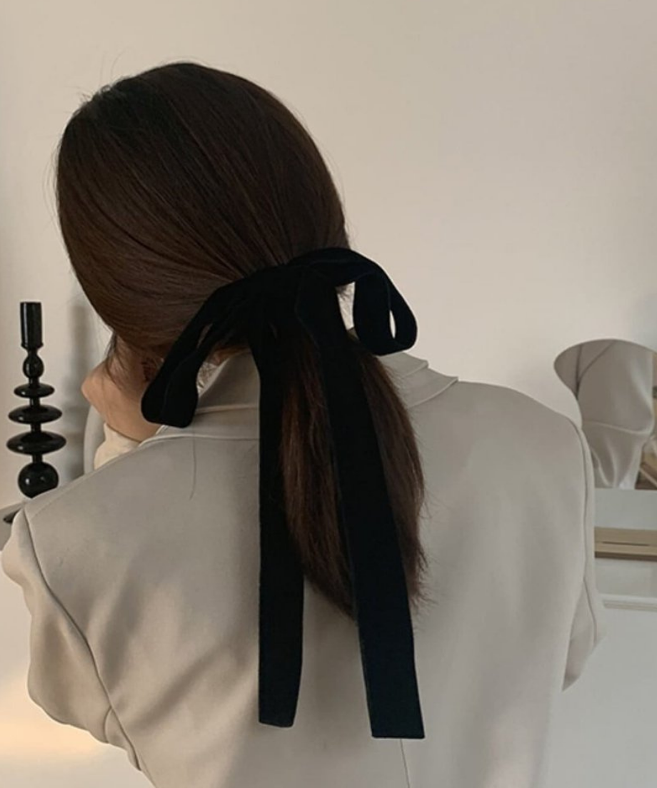 ベージュのジャケットを着用した女性が、黒のベルベットリボンで低めのポニーテールを作っている後ろ姿。
