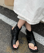黒のブーツサンダルを履いて足を交差させた、白いネイルが映える足元のクローズアップ