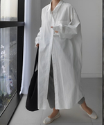 白いロングシャツワンピースを羽織り、グレーのパンツと白いフラットシューズで歩く女性の全身。