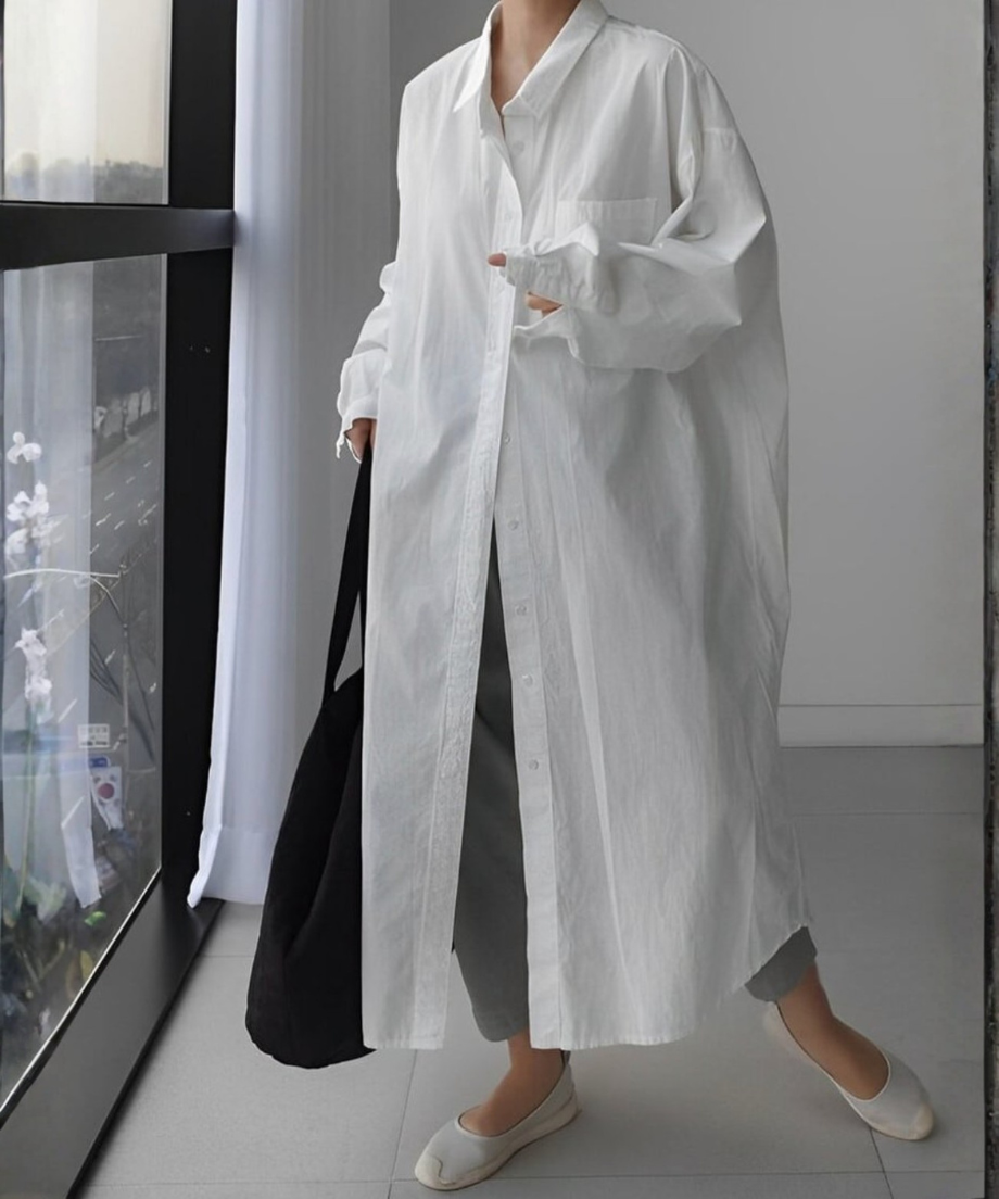 白いロングシャツワンピースを羽織り、グレーのパンツと白いフラットシューズで歩く女性の全身。
