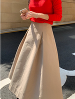 赤い長袖ニットとベージュのミディ丈フレアスカートを着用した女性の半身。