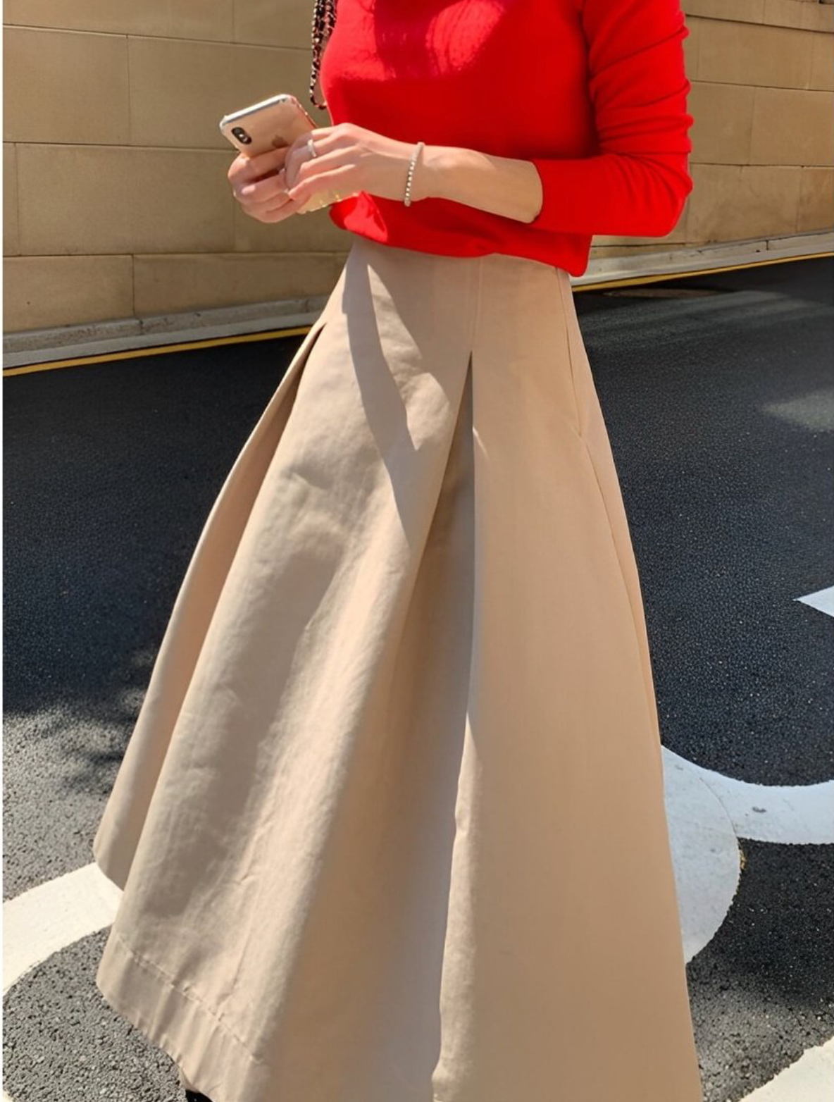 赤い長袖ニットとベージュのミディ丈フレアスカートを着用した女性の半身。