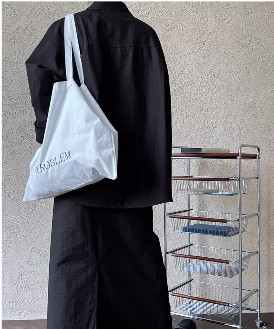 ブラックのシャツとロングスカートを着用した後ろ姿。白いトートバッグを肩にかけたワントーンコーデ。