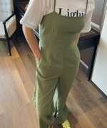 白いロゴTシャツの上にグリーンのキャミソールフレアジャンプスーツを重ね着し、ゴールドのパンプスを合わせた女性のクローズアップ。