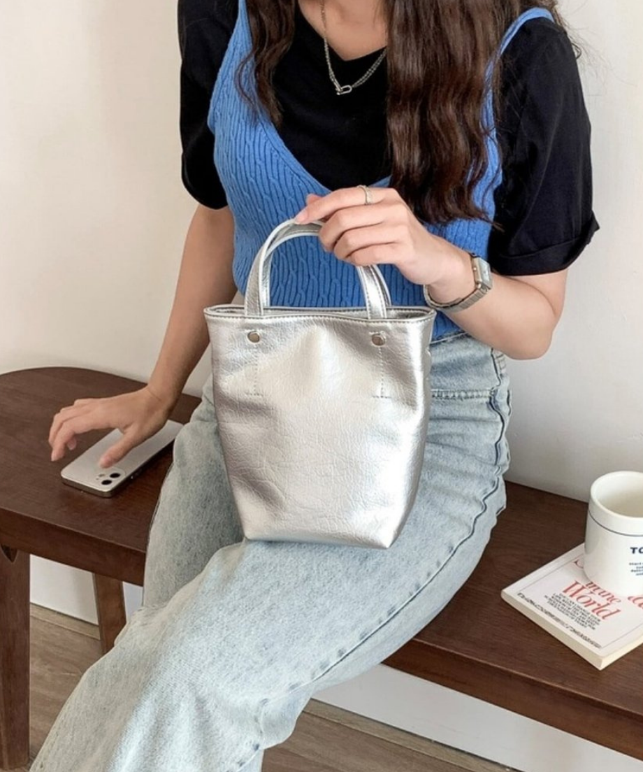 シルバーのミニトートバッグを手にする、ブルーのビスチェとデニムパンツを履いた女性