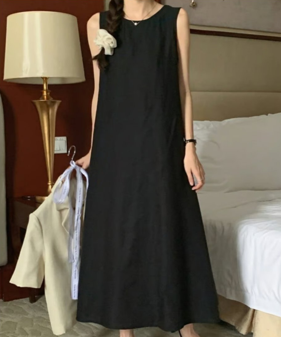 ブラックのロングワンピースを着用し、白いジャケットを手に持つ女性の立ち姿
