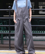 淡いブルーの半袖Tシャツにグレーのワイドレッグオーバーオールを着用し、正面を向いて立つ女性の全身写真。