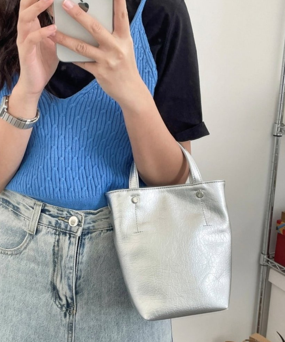 シルバーのミニトートバッグを腕にかけて鏡越しに自撮りをする女性
