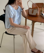 カフェのような空間で椅子に座る女性と、その横のテーブルに置かれたブラウンのキャンバスバッグ。