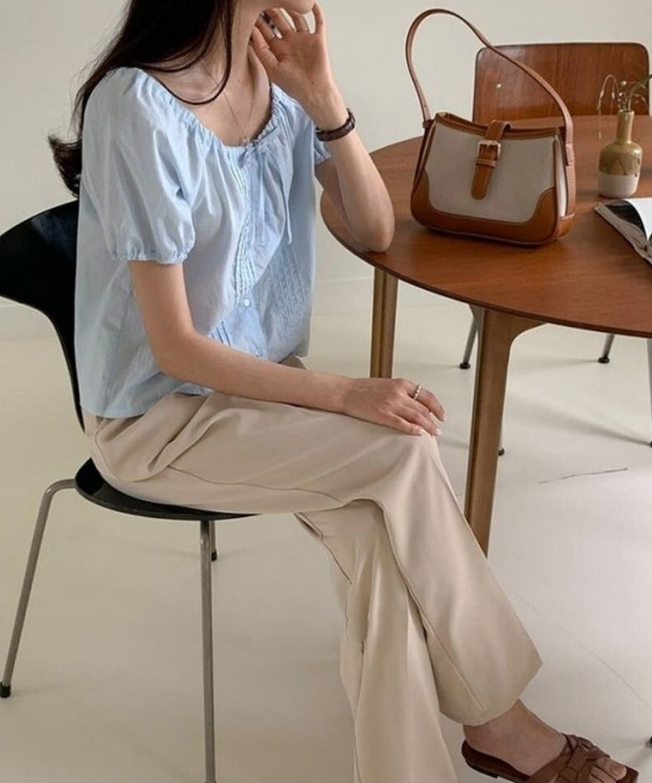 カフェのような空間で椅子に座る女性と、その横のテーブルに置かれたブラウンのキャンバスバッグ。