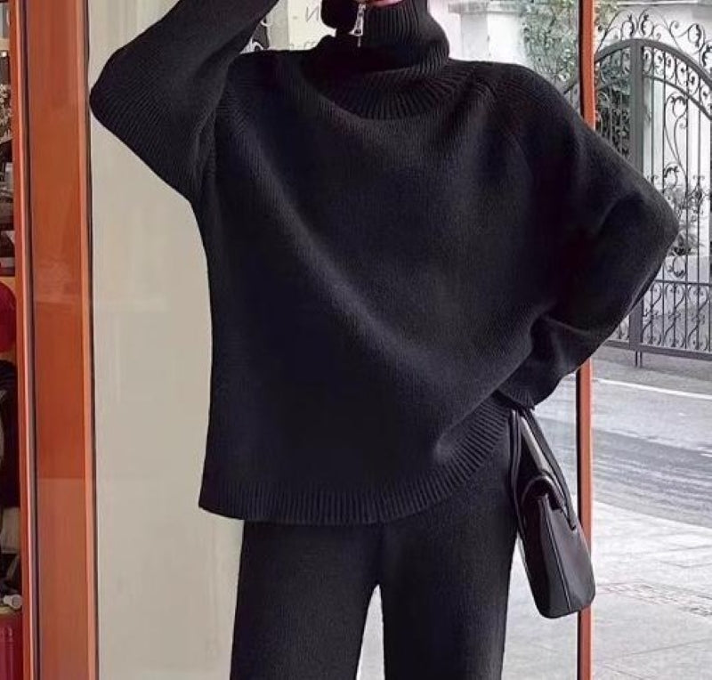 ブラックのニットセットアップを着た人物のクローズアップ画像。リラックスしたポーズを取っている。
