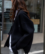 黒いオーバーサイズカーディガンを白いロゴTシャツに合わせた女性。