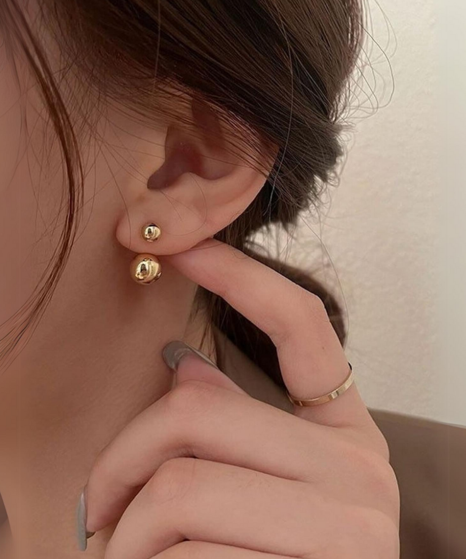 ゴールドのダブルボールピアスを着用し、指でピアスに触れている女性の手元