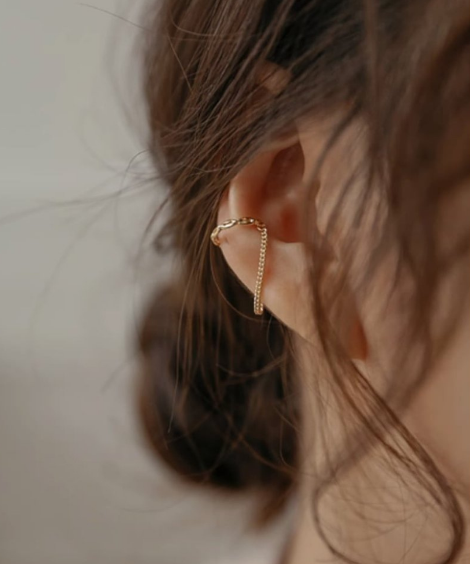 女性の耳の中央に装着された、ツイストデザインのリングからチェーンが垂れ下がるゴールドイヤーカフの着用画像。