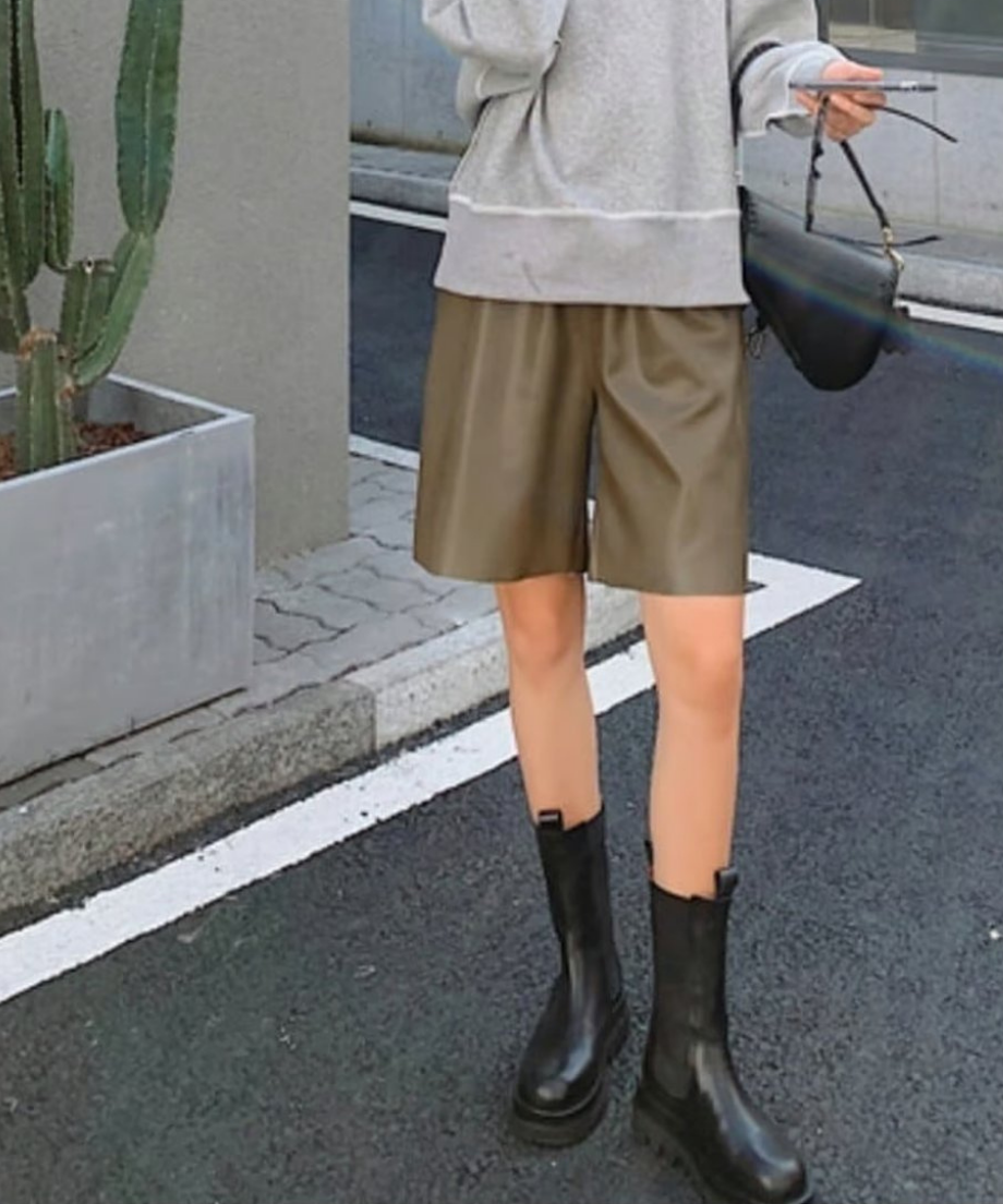 オリーブ色のエコレザーショーツにグレーのオーバーサイズスウェットと黒のショルダーバッグを合わせた、リラックス感のある大人カジュアル。