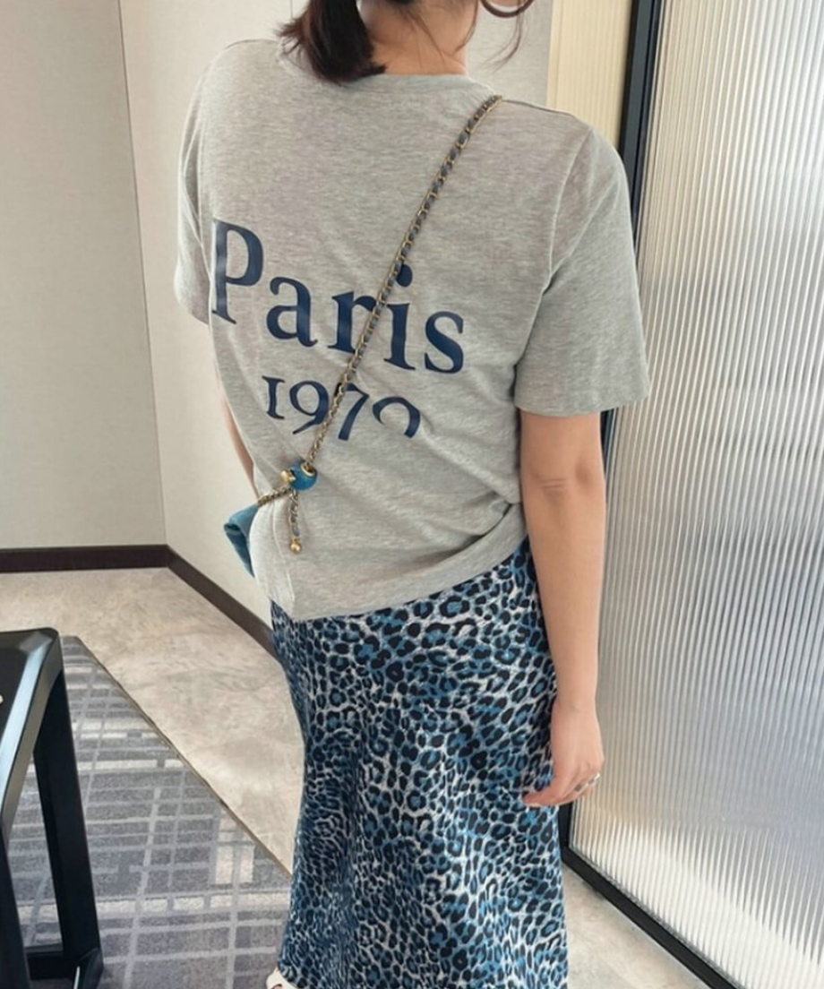 グレーの「Paris 1970」ロゴTシャツとブルーのレオパード柄ロングスカートを合わせたバックスタイル。