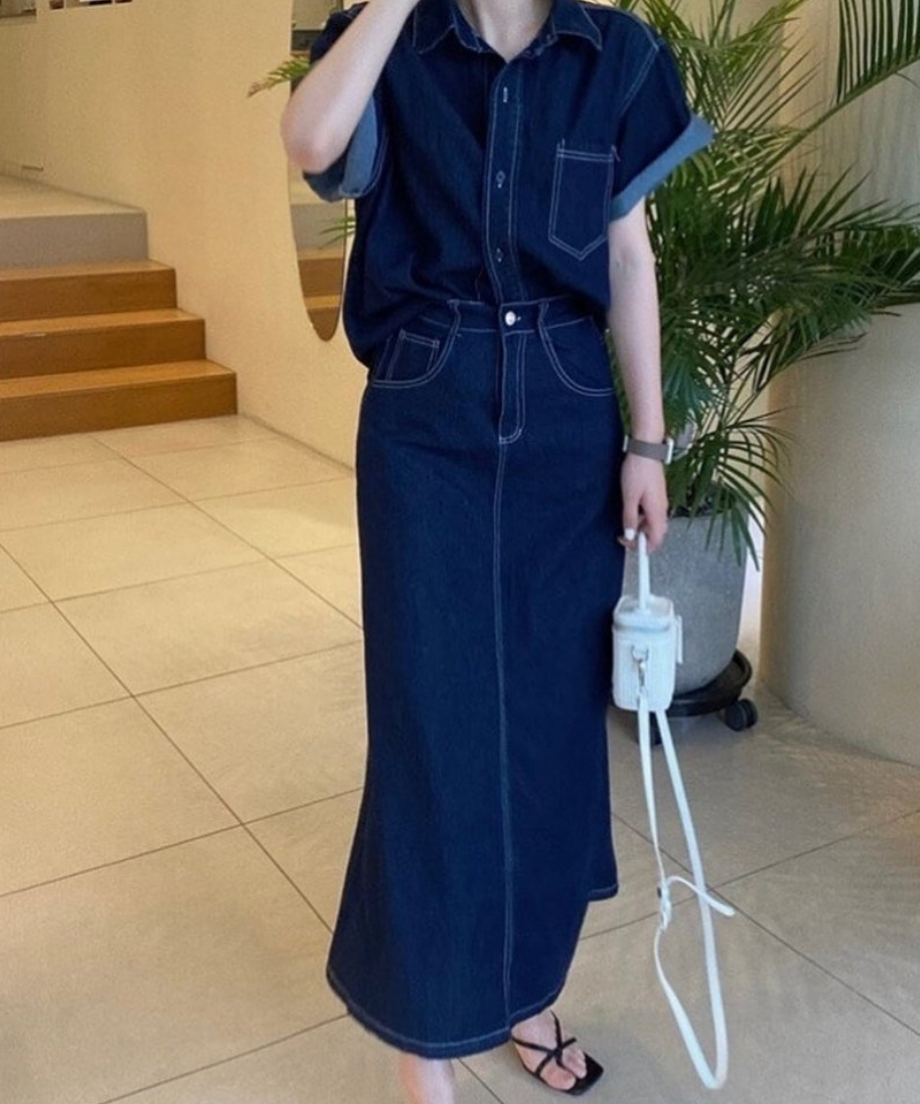 濃紺のデニムセットアップを着用した女性の全身像。黒の細いストラップサンダルを履いている。