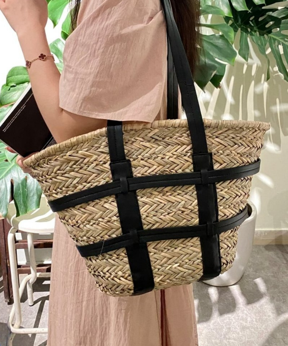 植物の横でモデルが肩に掛けた、夏らしい爽やかなコーディネートのブラックストローバッグ。