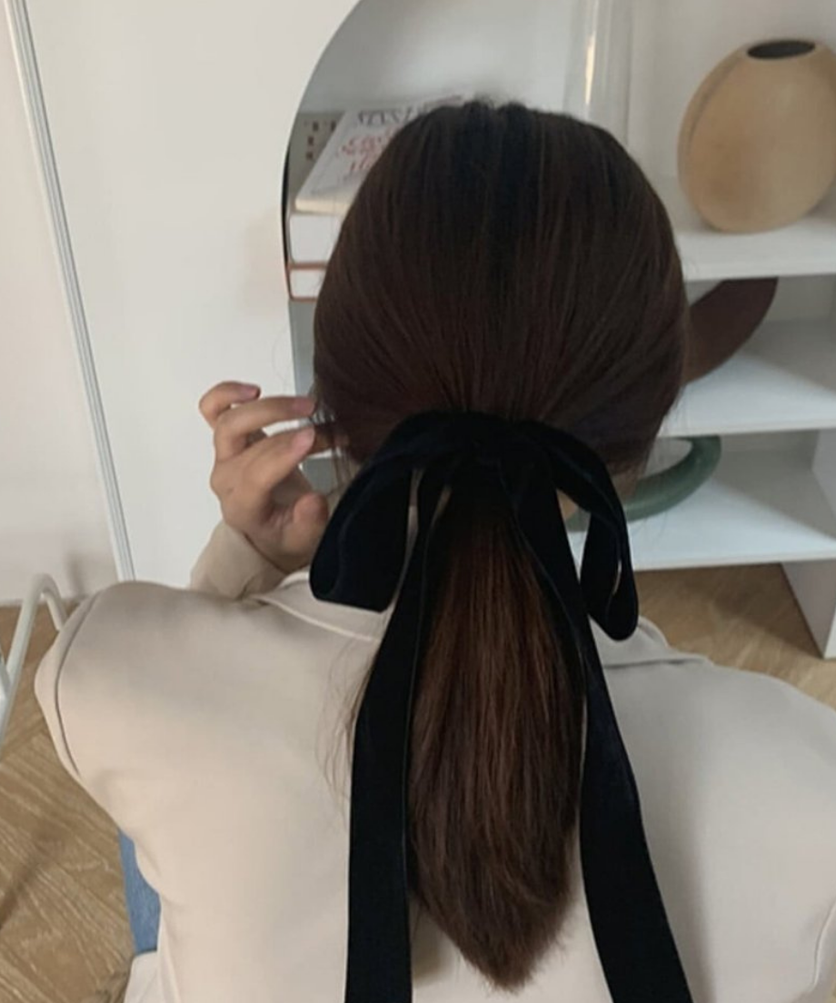 ベージュのジャケットを着用した女性が、黒のベルベットリボンで低めのポニーテールを作っている後ろ姿。
