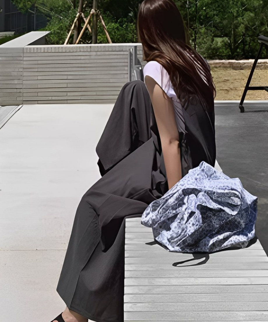 グレーのサロペットを着た女性が、柄物のバッグを置いて座っている写真。