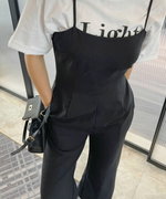 白いロゴTシャツの上に黒のキャミソールフレアジャンプスーツを重ね着し、黒のショルダーバッグを持った女性の上半身。