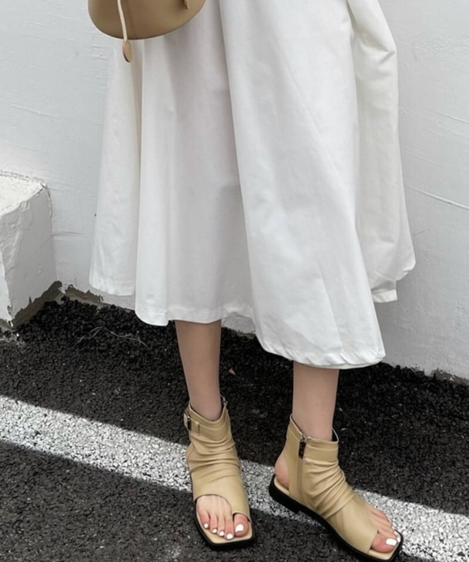 白いロングスカートとベージュのシャーリングブーツサンダルを合わせた女性の立ち姿。