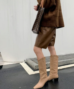 ブラウンのハーフパンツとロングブーツを着用し、モノグラム柄のトートバッグを持った横向きのスタイリング。