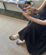 黒いマキシワンピースを着用した女性の足元に映えるオフホワイトのメタルサンダルのサイドスタイル。