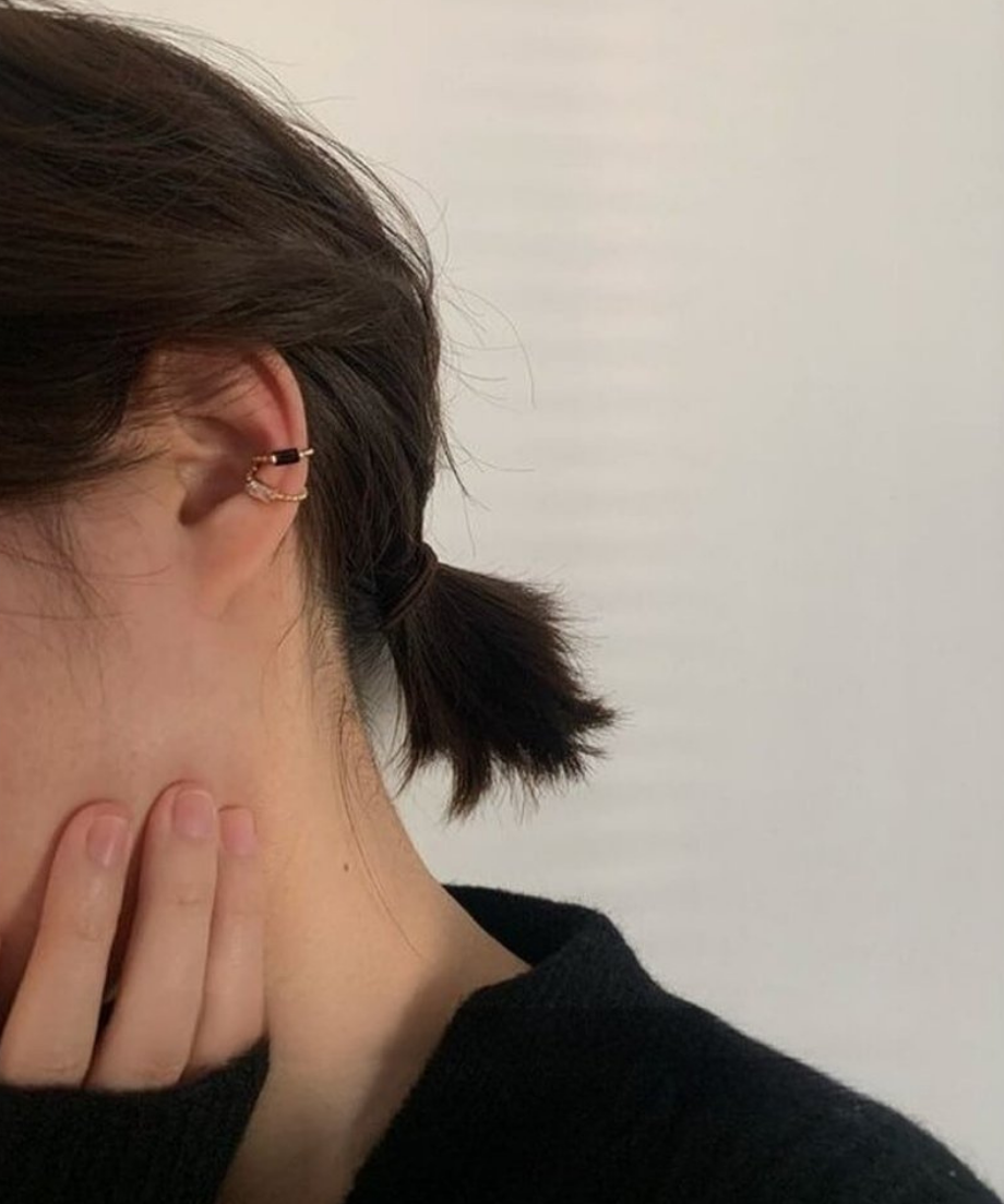黒いトップスを着用した女性の耳元を飾る、シックでモダンな印象のイヤーカフスタイリング。