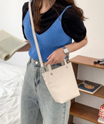 ホワイトのミニトートバッグを肩掛けにして本を持つ、デニムスタイルの女性の全身カット