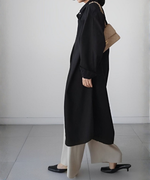 黒いロングシャツワンピースを羽織り、ベージュのワイドパンツと黒いローヒールサンダルを合わせた女性が歩いている横向き全身。