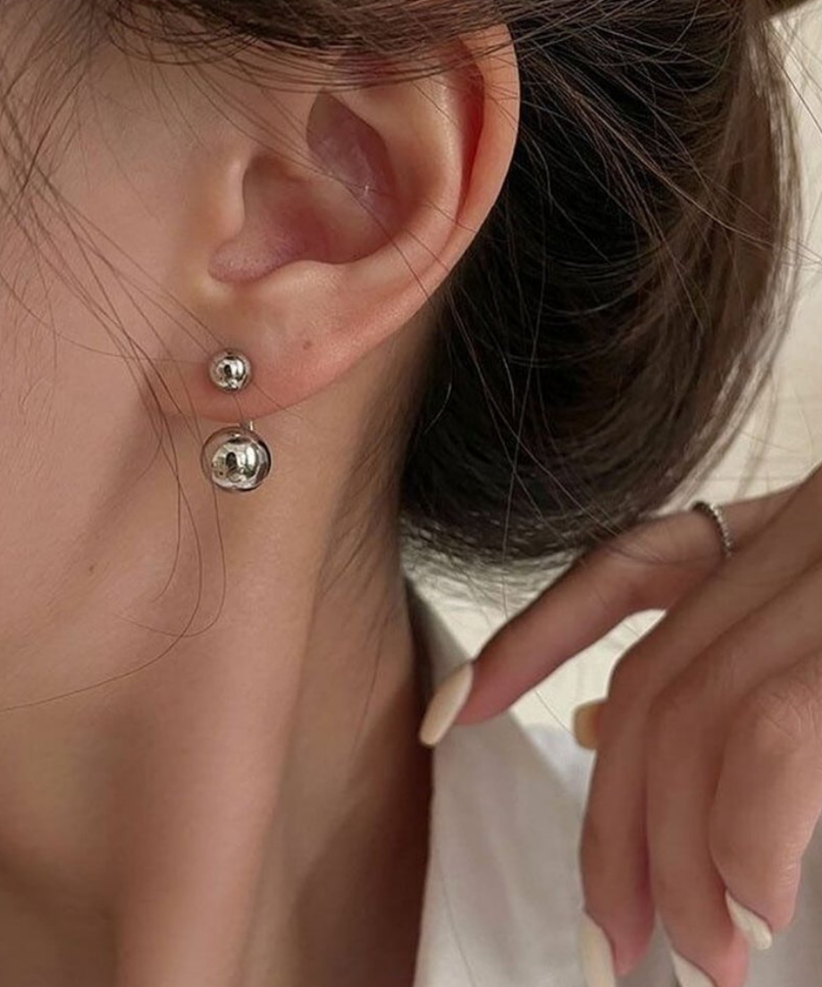 耳元にシルバーのダブルボールピアスを着用し、髪を耳にかけた女性の横顔
