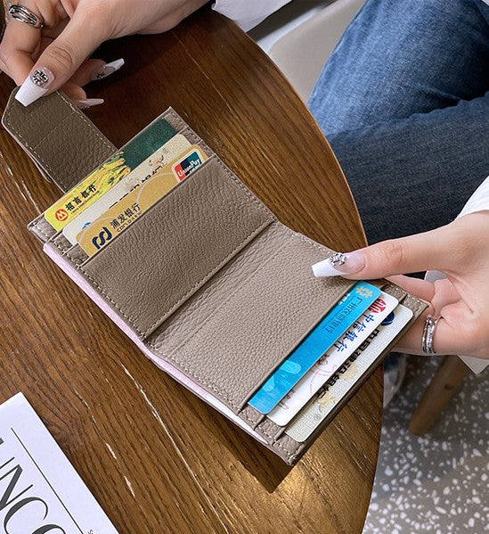 グレーのスリムな二つ折り財布を開き、内側のカードスロットに複数のカードが収納されている様子を、ネイルをした手が持っている写真。