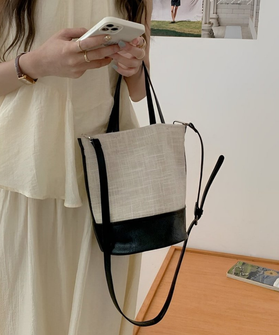 バッグを肩にかけながらスマートフォンを操作する女性の横姿。
