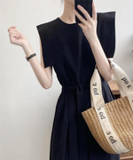 黒のオールインワンにカゴバッグを合わせた女性の全身像。ポーズをとっている。