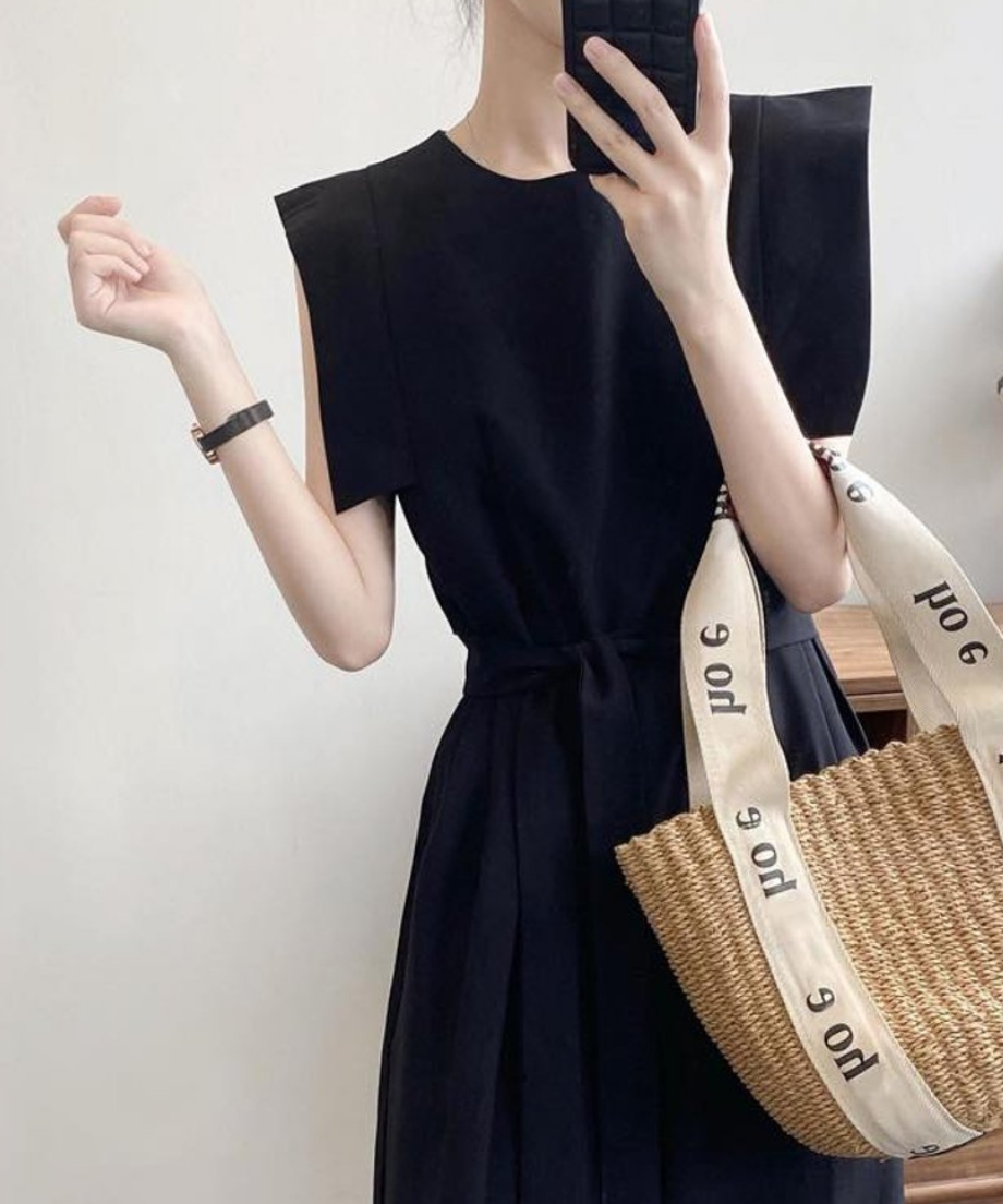 黒のオールインワンにカゴバッグを合わせた女性の全身像。ポーズをとっている。