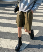 サドル型の黒いバッグを肩にかけ、カーキのハーフパンツとグレーのスウェットを合わせた都会的なスタイル。