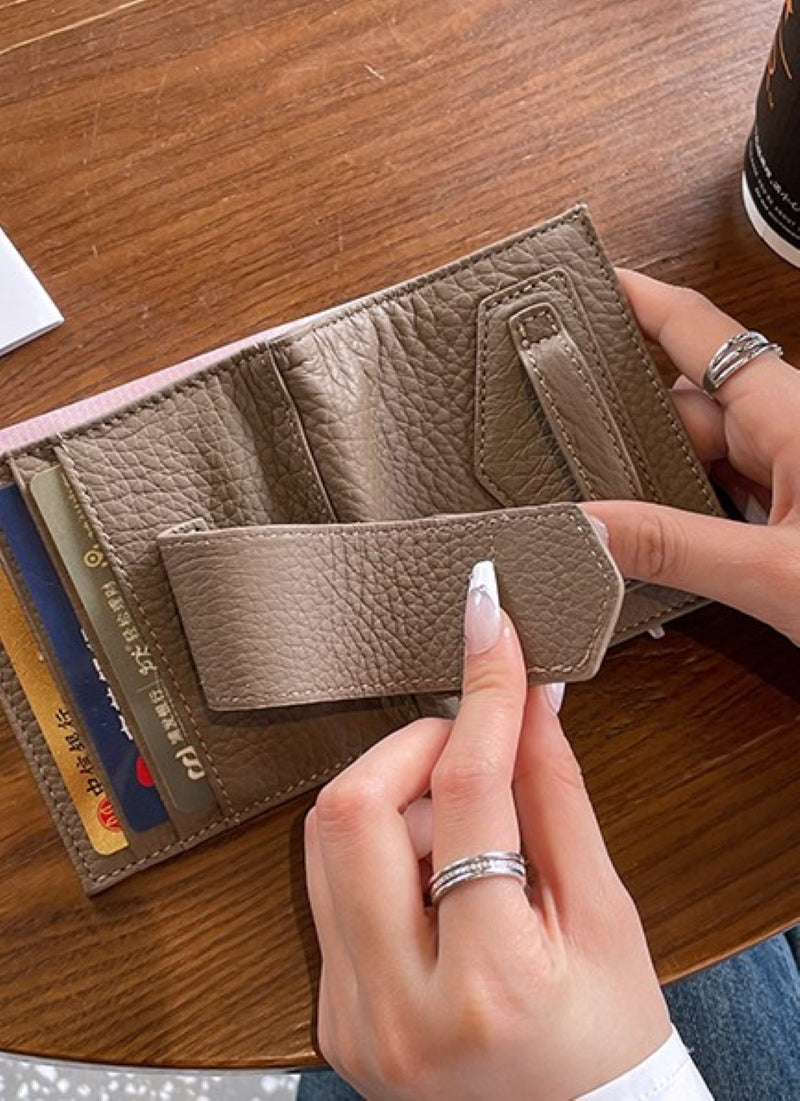 グレーのスリムな二つ折り財布を開き、内側のカードスロットとフラップの留め具部分を、ネイルをした手が操作している接写写真。