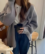 グレーのオーバーサイズカーディガンを白いTシャツ、濃紺のデニムパンツに合わせ、黒いマグカップを持つ女性の上半身。