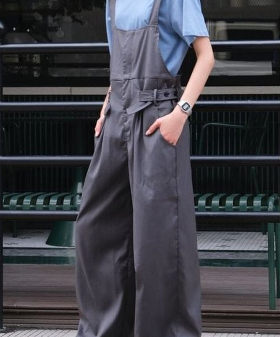 淡いブルーの半袖Tシャツにグレーのワイドレッグオーバーオールを着用し、正面を向いてポーズをとっている女性の全身写真。