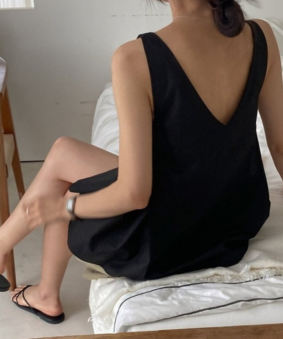 ベッドに腰掛け、ブラックのブラウスを着用した女性の斜め後ろからのスタイル