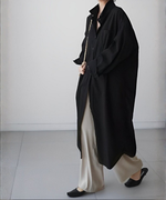 黒いロングシャツワンピースを羽織り、ベージュのワイドパンツと黒いローヒールサンダルを合わせた女性が歩いている横向き全身。
